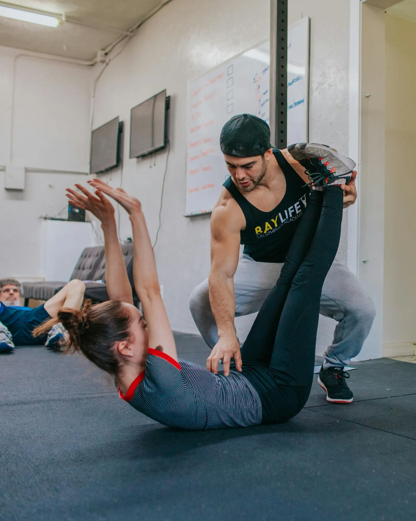 A trainer supports a person’s legs during a floor exercise on a mat