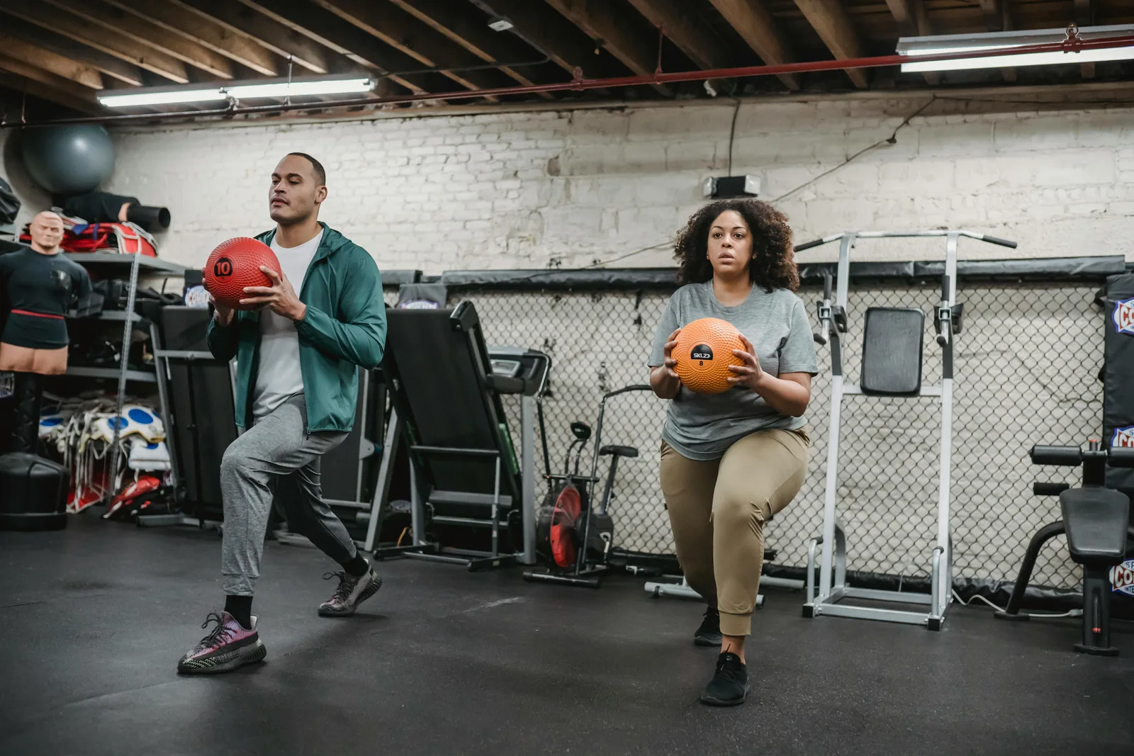 Two people lunging while holding medicine balls in a basement gym