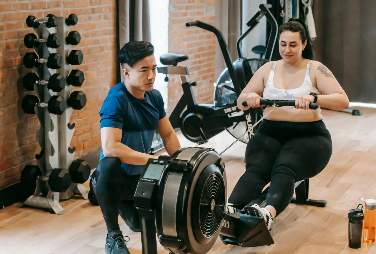 A man and a woman using a rowing machine and an air bike in a small condo gym