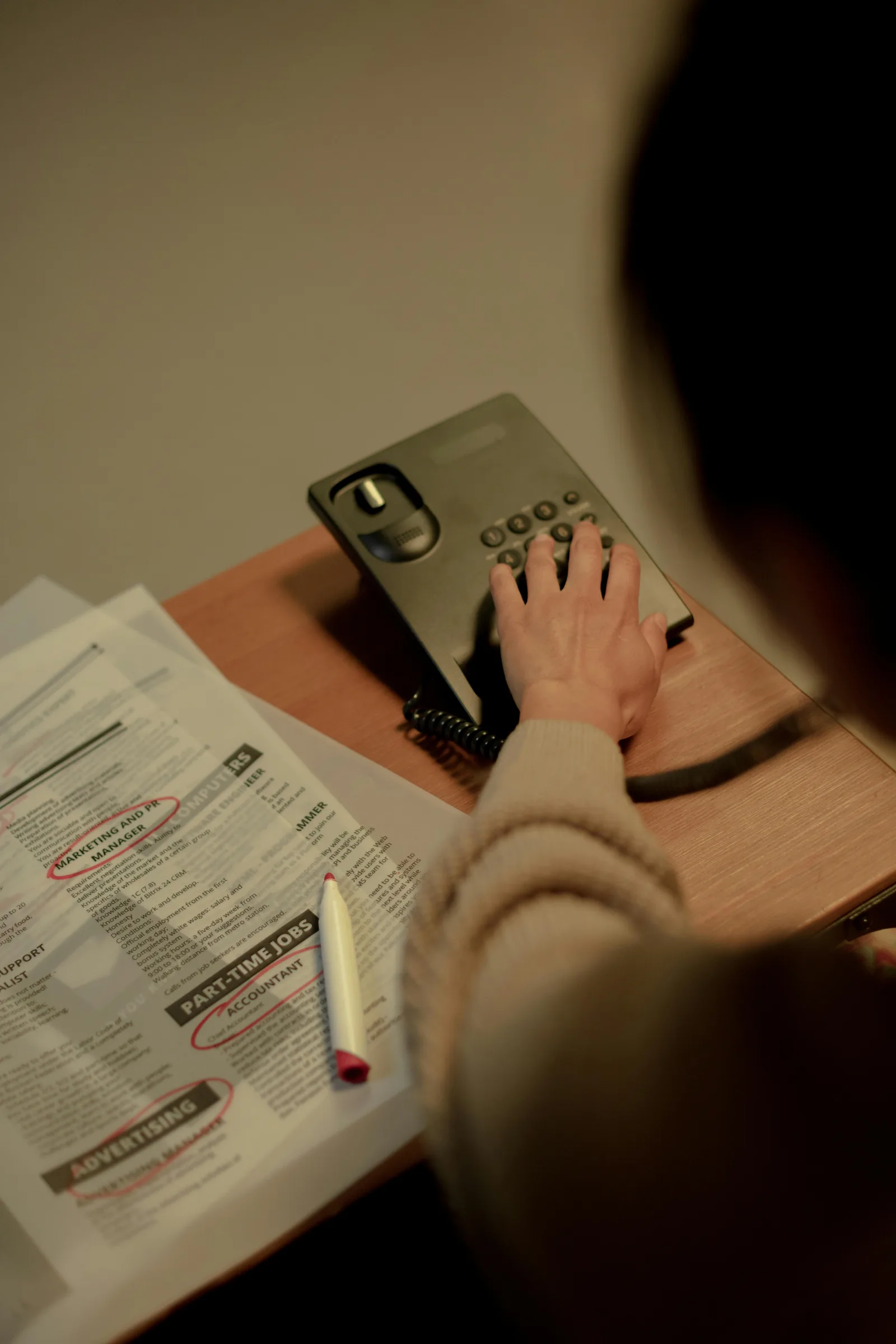 A hand holding a phone above printed pages and a pencil on a desk